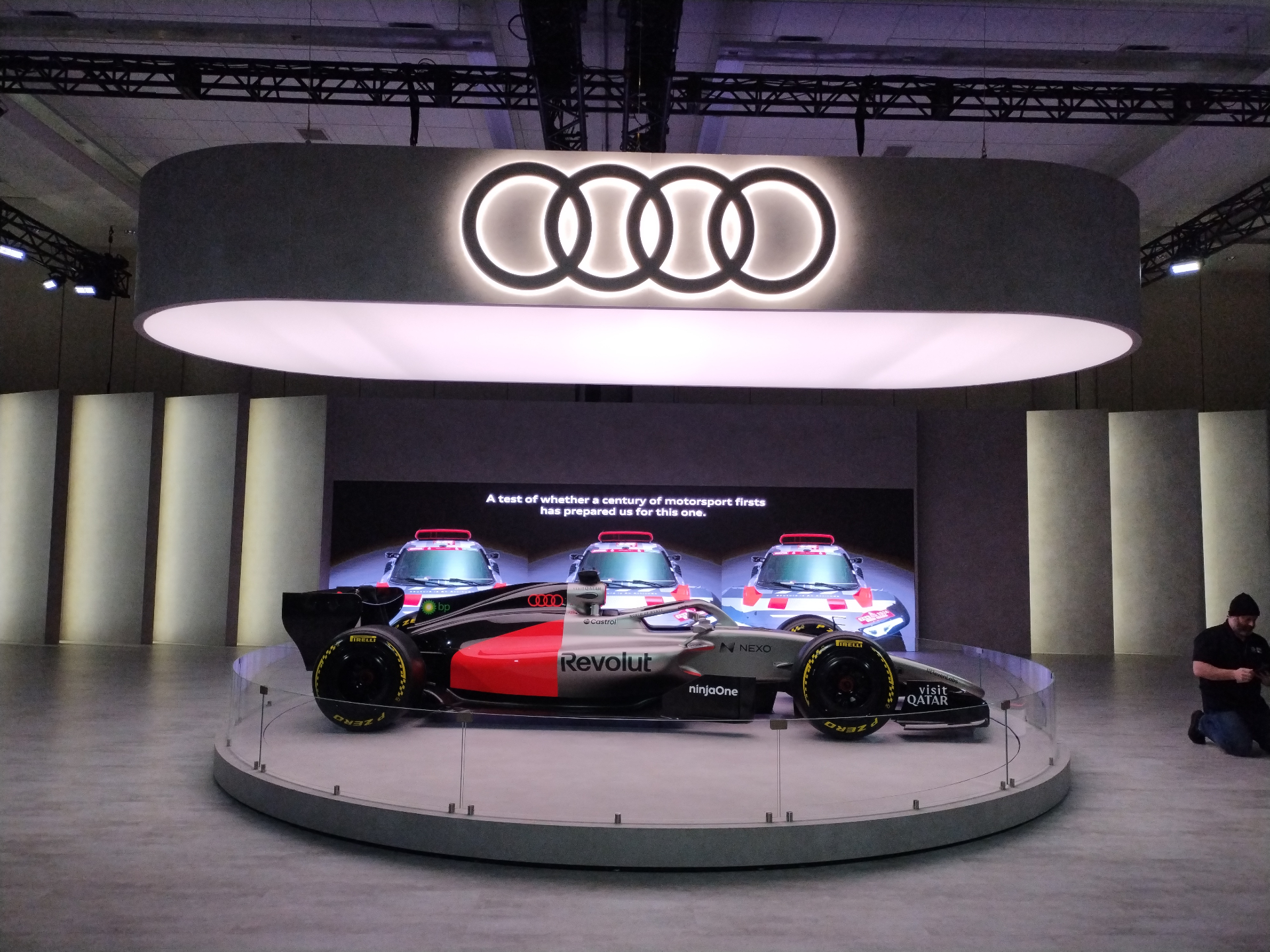 Event show floor with a vehicle display, illuminated overhead structure and digital backdrop
